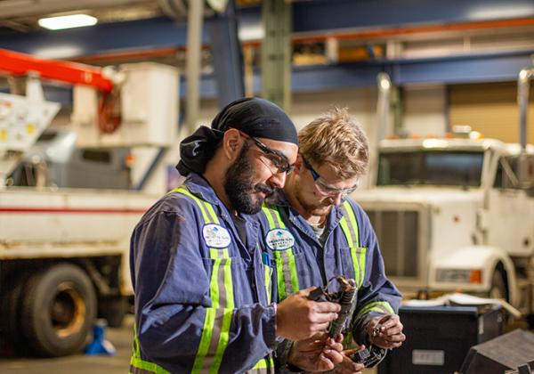 Two men in safety gear examining a mechanical piece togehter.